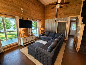 A log cabin interior with a sectional sofa, a flat-screen TV, and a ceiling fan. - Lakefront Paradise in Double Springs, AL 6BR Cabin with Private Dock (Double Springs)