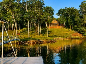 A lakeside property with a dock, a house on a grassy hill, and trees surrounding the area. - Lakefront Paradise in Double Springs, AL 6BR Cabin with Private Dock (Double Springs)
