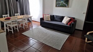 A living area with a sofa, a dining table with chairs, a rug, and a painting on the wall. - T1 University of the Azores P. Delgada (PONTA DELGADA)