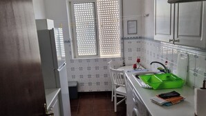 A compact kitchen with a washing machine, a sink, and a window with blinds. - T1 University of the Azores P. Delgada (PONTA DELGADA)