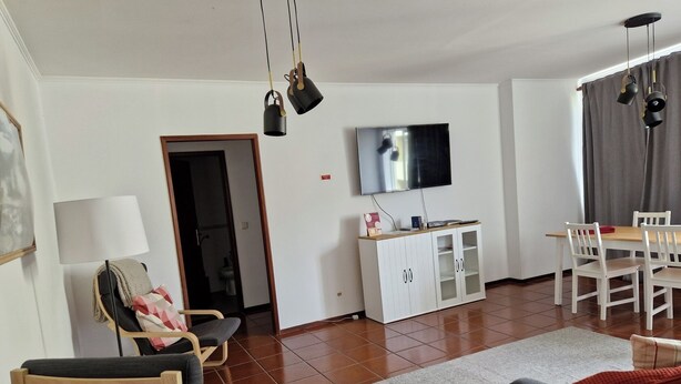 A living room with a TV, white furniture, a dining area, and a door leading to a bathroom. - T1 University of the Azores P. Delgada (PONTA DELGADA)