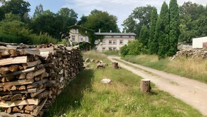 Un entorno rural con una casa, un sendero de tierra y leña apilada.