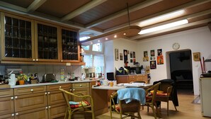Una cocina con armarios de madera, un comedor con sillas de mimbre y un reloj en la pared.