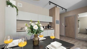 A modern dining area with a table set for two, a vase with flowers, and a kitchen in the background. - Modern Apartment with a Balcony | Pool, Spa, Gym (Międzyzdroje)
