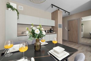 Un comedor moderno con una mesa dispuesta para dos, un jarrón con flores y una cocina al fondo.