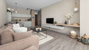 A modern living room with a sofa, coffee table, TV, and a kitchen in the background. - Modern Apartment with a Balcony | Pool, Spa, Gym (Międzyzdroje)