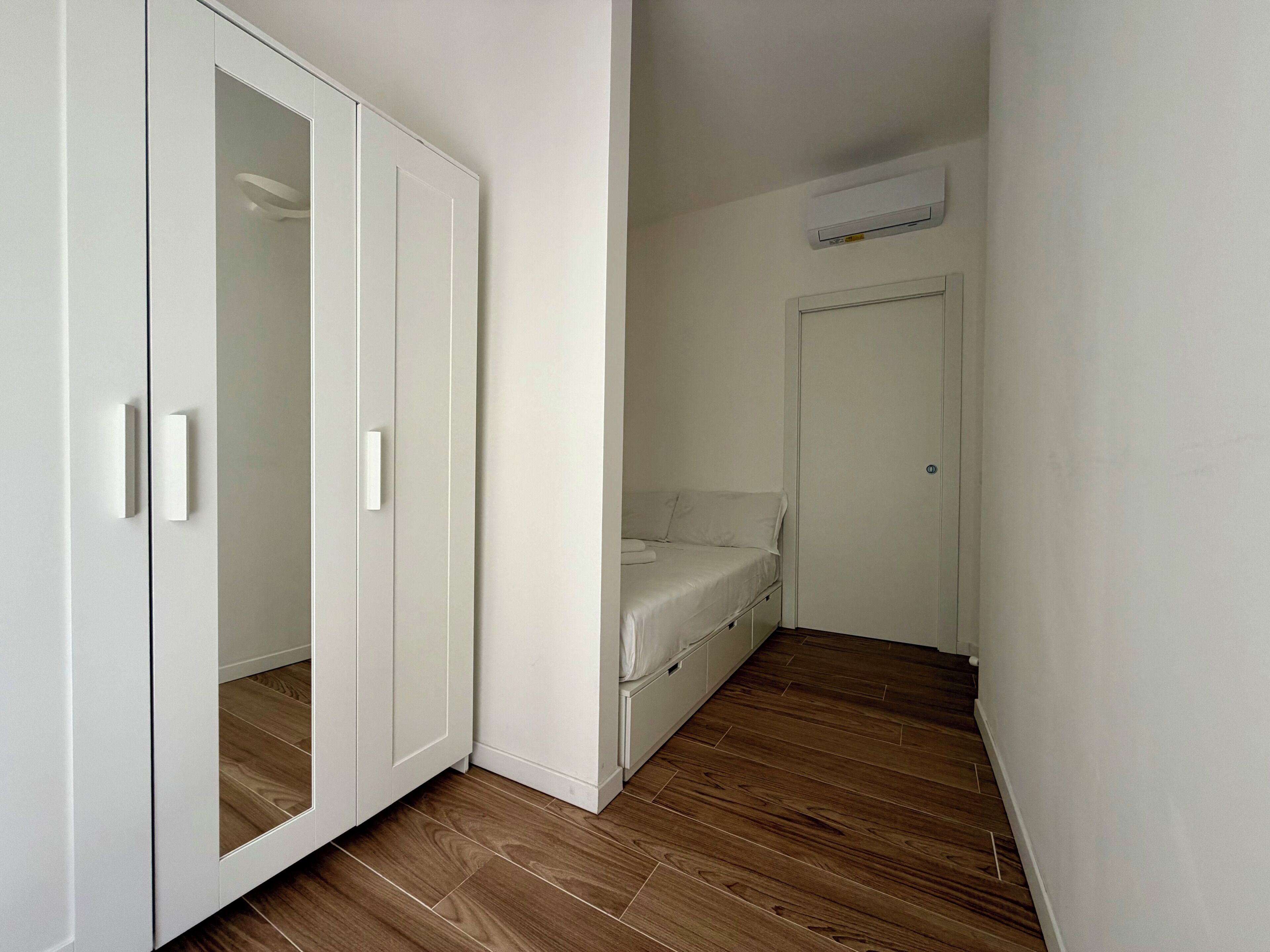A bedroom with a wardrobe, a bed, and an air conditioning unit.