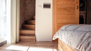 Un dormitorio con una escalera de madera, una cama con edredón gris y un termostato en la pared.