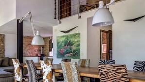 Uma sala de jantar com mesa e cadeiras de madeira, uma luminária pendente grande e uma parede de pedra.
