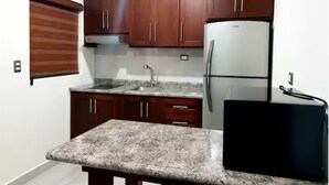 A kitchen with granite countertops, wooden cabinets, a stainless steel refrigerator, and a black appliance on the right. - Luxury apartment #4 steps away from IMSS / UMAE (Ciudad Obregón)