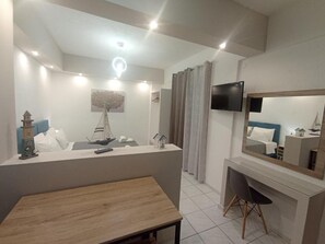 Ein modernes Hotelzimmer mit Schreibtisch aus Holz, einem an der Wand befestigten Fernseher, einer Bootsdekoration und einem großen Spiegel, der den Raum reflektiert.