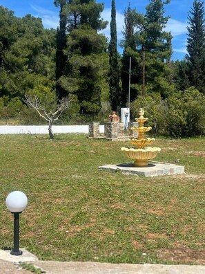 Ein Springbrunnen in einem Park mit einem weißen Zaun und Bäumen im Hintergrund.