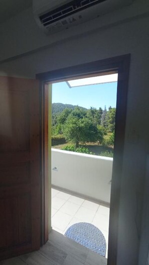 Ein Zimmer mit Holztür, Fliesenboden und Blick auf eine Straße und Grünfläche.