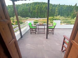 Eine Terrasse im Freien mit Tisch und Stühlen, einer Brüstung und Blick auf ein bewaldetes Gebiet.