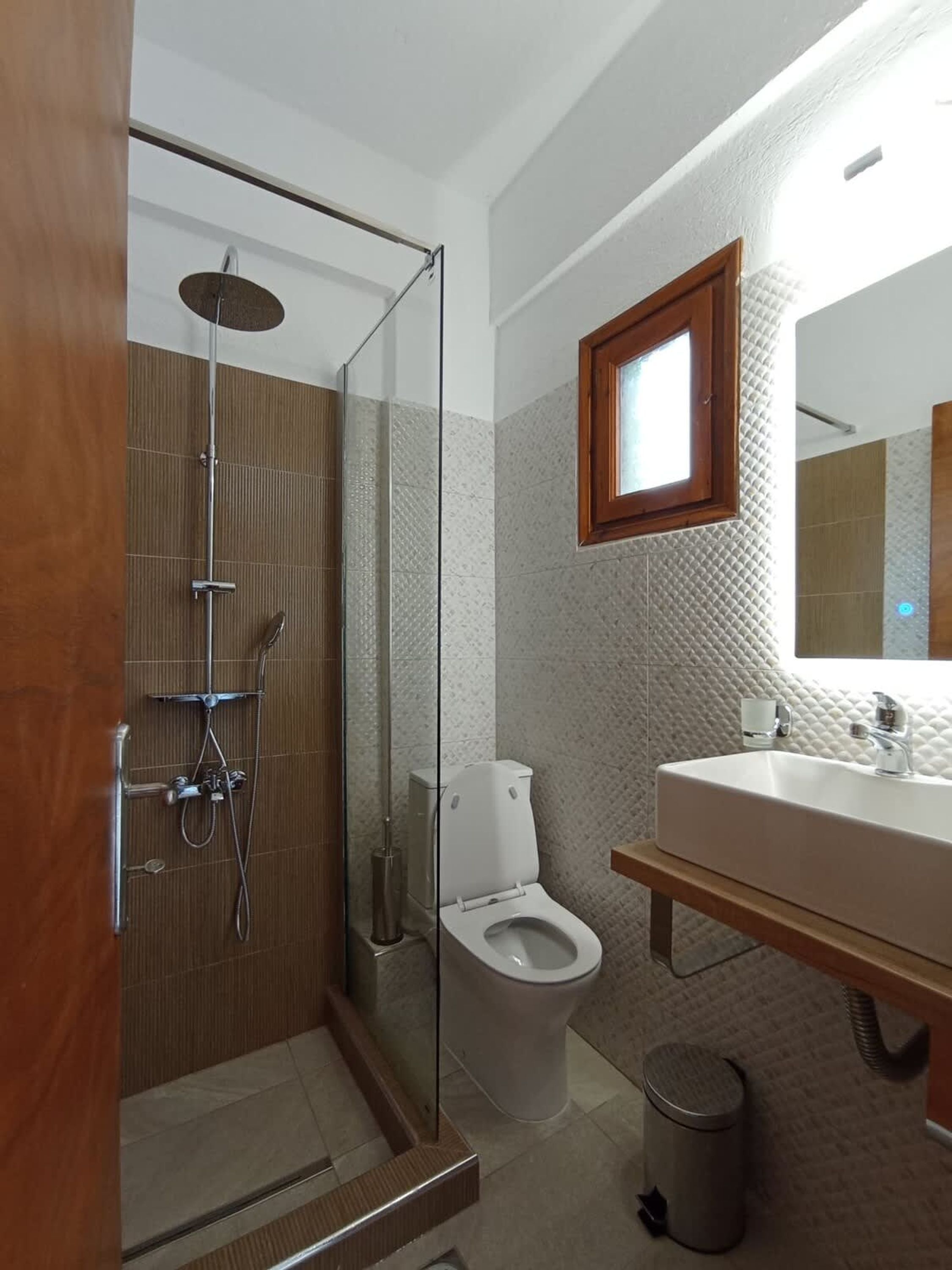 A modern bathroom with a glass-enclosed shower, a toilet, and a sink with a mirror above.