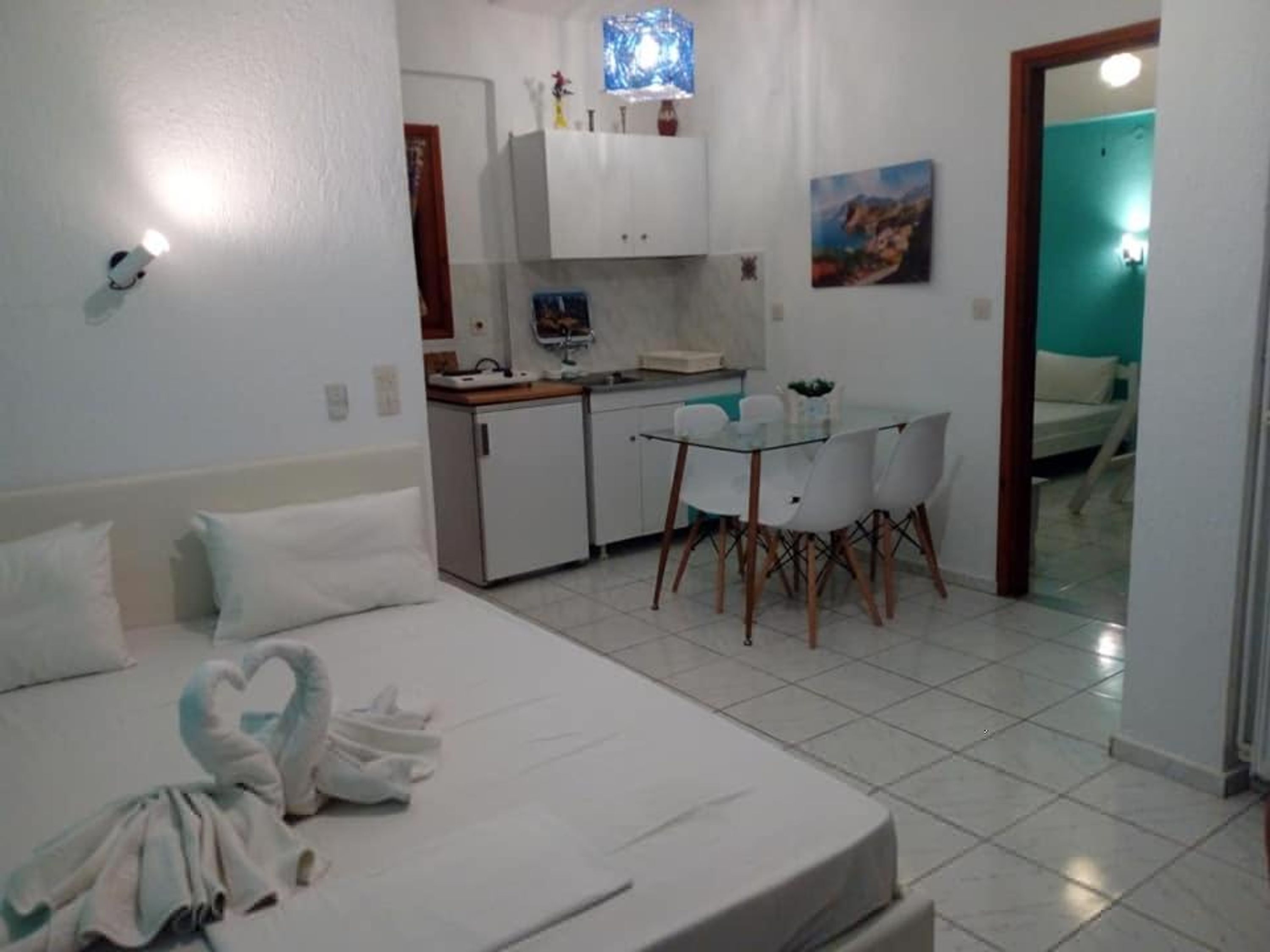 A hotel room with a bed, a small kitchenette, a dining table with chairs, and a bathroom visible through an open door.