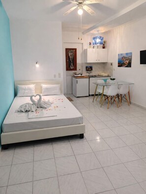 Ein Schlafzimmer mit einem Bett, einem Schreibtisch, einem Stuhl, einem Deckenventilator und einer Küchenzeile.