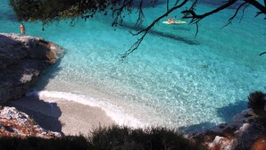 A coastal scene with clear turquoise water, a rocky shoreline, and a person standing on a cliff. - Skopelos Cozy Escape Near The Forest the Sea (Skopelos)