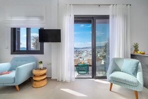 Una sala de estar moderna con un sofá, una butaca, un televisor y vistas a un paisaje urbano a través de un ventanal.