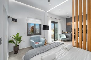 Un dormitorio moderno con cama, dos sillas, televisión y balcón con vistas.
