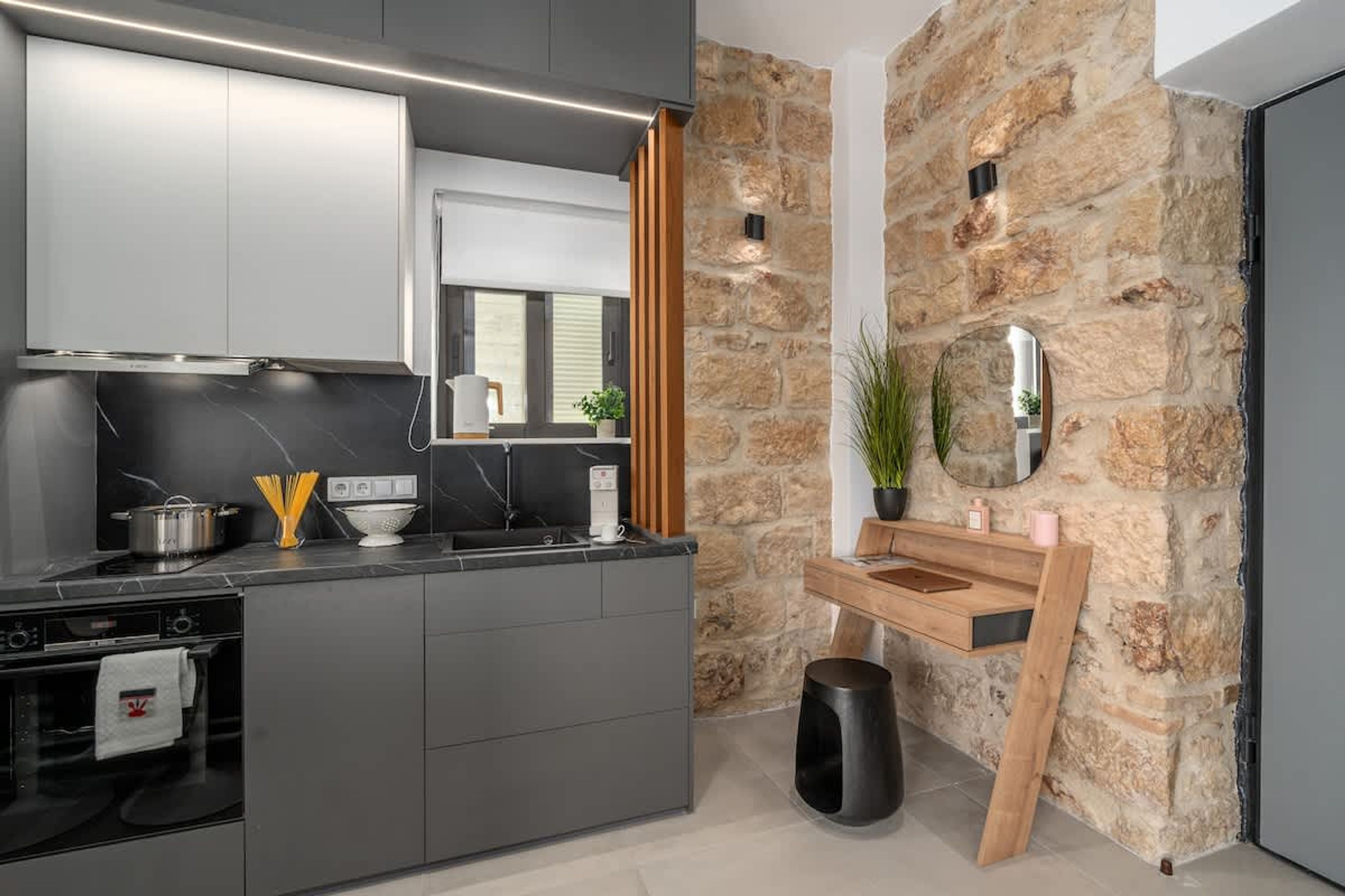 Una cocina moderna con armarios grises, encimera negra, pared de piedra e banco de madera.