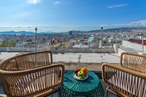 A rooftop terrace with wicker chairs, a small table with fruit, and a city view. - Green Blue Castella Luxury Suites Odyssey Suite (Piraeus)