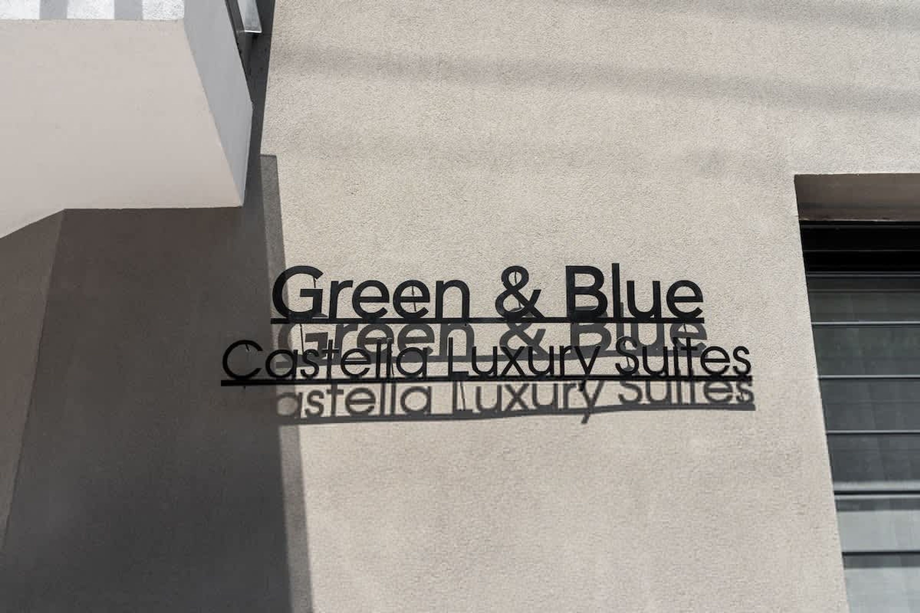 Une façade d’immeuble portant l’inscription « Green & Blue Castella Luxury Suites », qui indique le nom de l’hôtel ou de l’établissement.