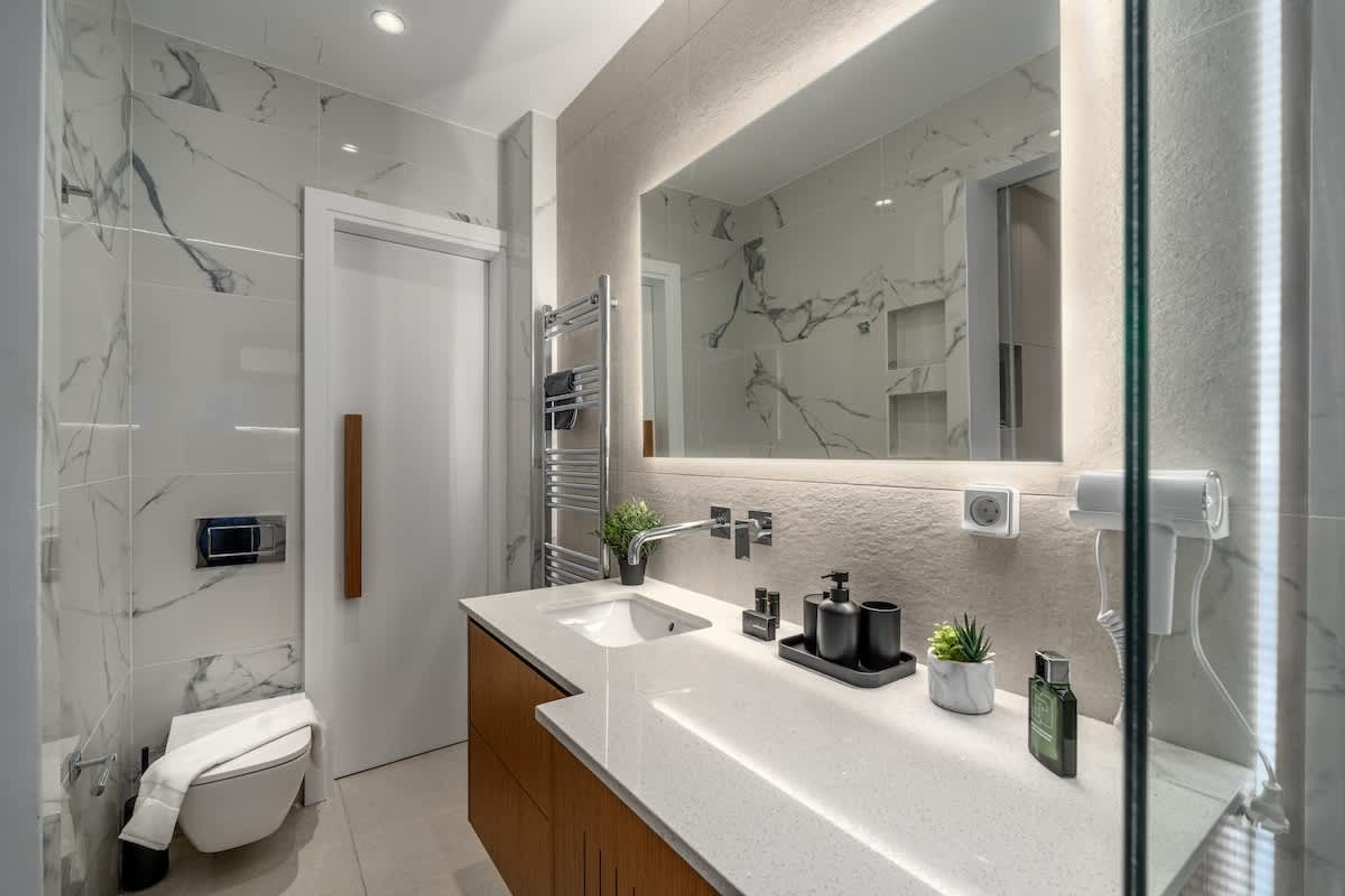 Une salle de bain moderne avec un pare-baignoire en marbre, un grand miroir, un meuble-lavabo à deux vasques et des toilettes.