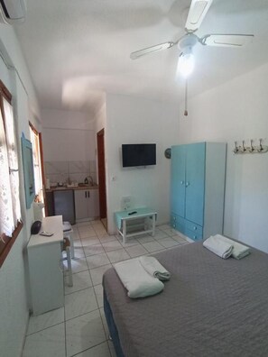 Ein Schlafzimmer mit einem Bett, einem Schreibtisch, einem Fernseher, einem Kleiderschrank und einem Deckenventilator.