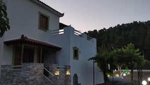 Un edificio de dos pisos con una escalera de piedra, un balcón y vistas a una colina boscosa.