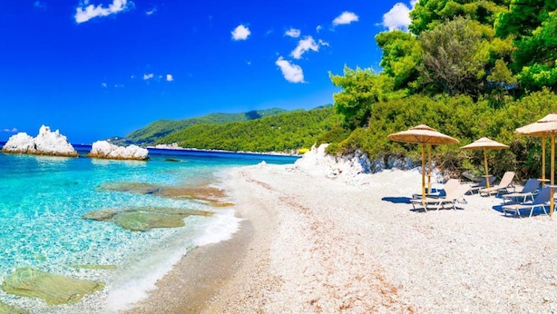 Una playa con agua turquesa cristalina, arena blanca y una pequeña isla en la distancia.