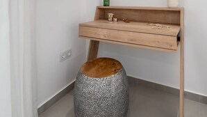 A bathroom with a wooden vanity, a round mirror, a television mounted above the vanity, a small stool, and a potted plant. - Green Blue Castella Luxury Suites Saronic Pearl (Piraeus)