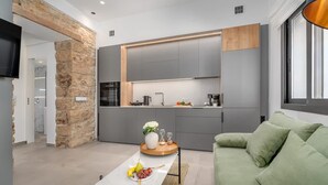 A modern kitchen with grey cabinets, a stone accent wall, and a dining area with a green sofa. - Green Blue Castella Luxury Suites Saronic Pearl (Piraeus)