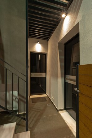 Un couloir étroit, avec un escalier sur la gauche, une porte sur la droite et une source de lumière au fond du couloir.