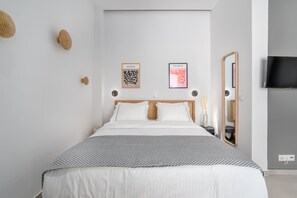 Une chambre moderne avec un lit, deux œuvres d’art accrochées au mur, un miroir et un téléviseur.