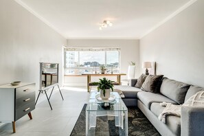 A modern living room with a sofa, coffee table, TV, and a view of the city. - Stylish Green Point 2 Bed w Views Rockaway Haven (Cape Town)