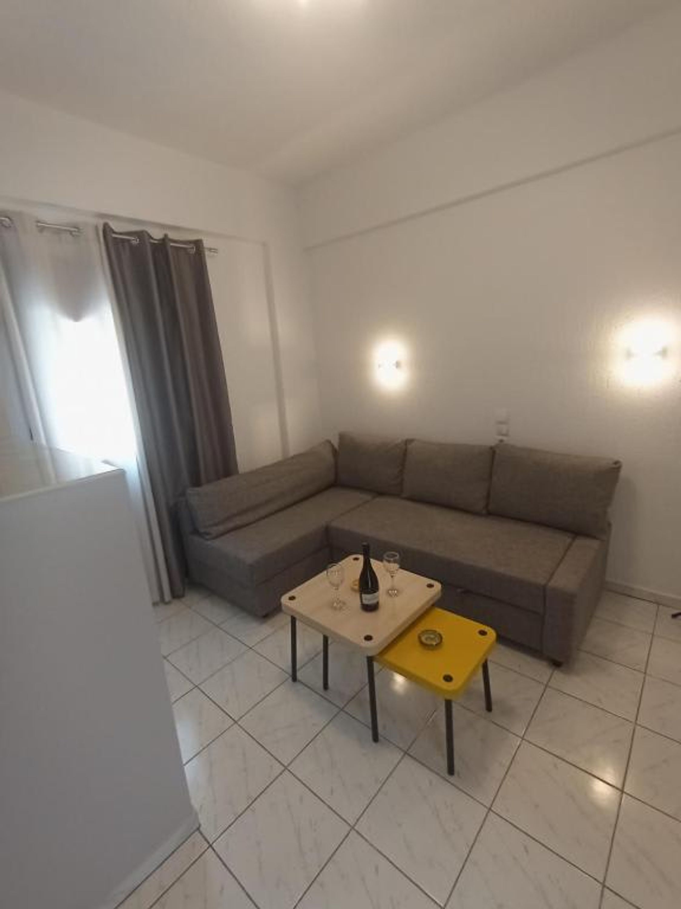 A living room with a sectional sofa, a small table with a bottle and glasses, and a yellow ottoman.