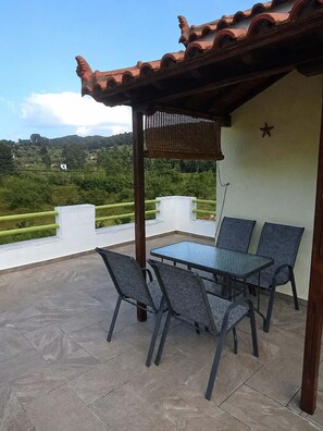 Eine Terrasse mit Tisch und Stühlen, einer Pergola und Blick auf eine grüne Landschaft.
