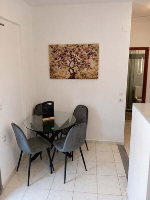 Ein Essbereich mit einem Glastisch, vier Stühlen, einem Wandbild und einer Tür zu einer Dusche.