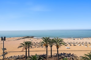Una platja amb palmeres, ombrel·les i cadiretes de platja.