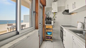 Uma cozinha compacta com vista para o mar, micro-ondas, cafeteira e máquina de lavar louça.