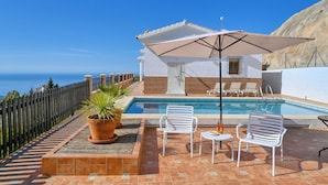 A pool area with a view of the sea, a covered seating area, and a wooden fence. - Kousgaard - Spacious private villa in quiet area with pool and sea view (Sayalonga)