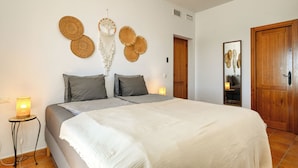 A bedroom with a bed, pillows, a bedside lamp, a wall hanging, and a door. - Kousgaard - Spacious private villa in quiet area with pool and sea view (Sayalonga)