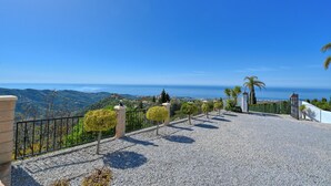 A gravel pathway with a metal fence, a stone pillar, and a view of the sea and hills. - Kousgaard - Spacious private villa in quiet area with pool and sea view (Sayalonga)