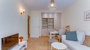 Ett modernt vardagsrum med en platt-TV, en vit soffa, ett matbord med stolar och en hängande lampa.