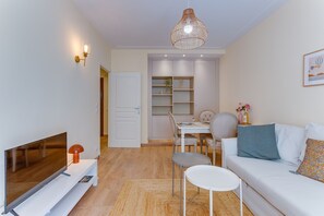 A modern living room with a flat-screen TV, a white sofa, a dining table with chairs, and a hanging light fixture. - L'Orangeraie AP4506 by Riviera Holiday Homes (Nice)