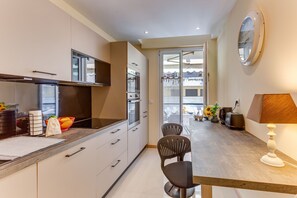 A modern kitchen with a dining area, a large mirror, and a view through a glass door. - L'Orangeraie AP4506 by Riviera Holiday Homes (Nice)