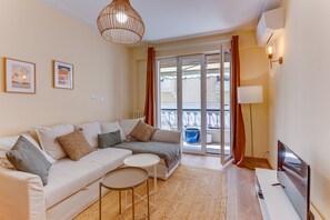 A modern living room with a sofa, a small table, a TV, and a balcony with a view. - L'Orangeraie AP4506 by Riviera Holiday Homes (Nice)