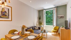 En matplats med ett bord dukat för två personer, en soffa, en tv och ett fönster med utsikt över grönområden.