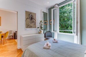 Ein Schlafzimmer mit Bett, Stuhl, Schreibtisch und einem Fenster mit Blick auf Bäume.